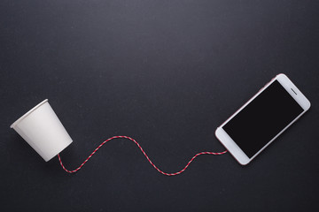 Two white paper cup connect with red rope used for classic phone and modern smartphone on black...