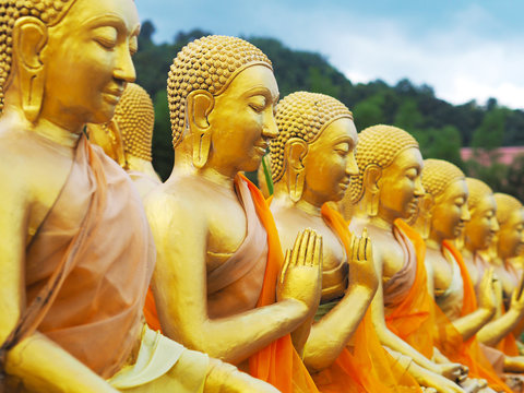 Row of golden monk statues sitting in various gestures at public temple in Nakornnayok province, Thailand.