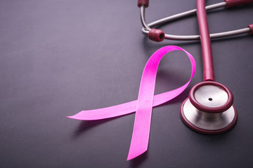 Breast Cancer concept : Pink ribbon symbol of breast cancer and doctor Stethoscope .on black stone...