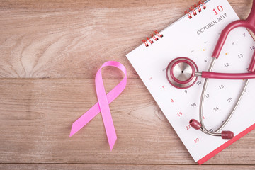 Breast Cancer concept : Pink ribbon symbol of breast cancer, calendar and stethoscope on brown wooden table. For breast/body checking appointment
