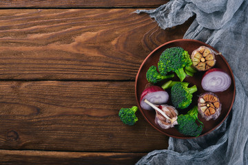 Fresh vegetables on a clay plate. On a wooden background. Top view. Free space for your text.