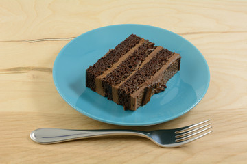 Slice of chocolate layer cake with chocolate icing on blue dessert plate with fork