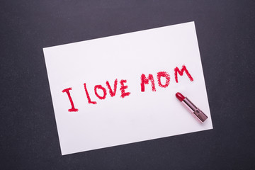 I LOVE MOM writing from red lipstick in white paper on black stone