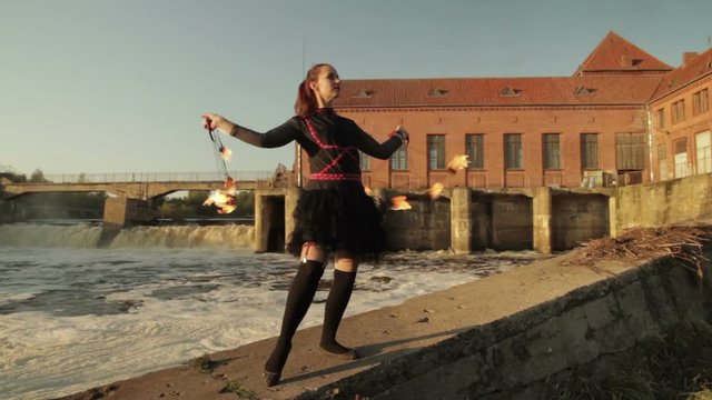 A young girl shows a fire show against the backdrop of an old German hydroelectric power station.