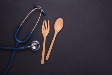 Blue doctor Stethoscope and set of spoon, fork and wooden dish on black stone board. Food and healthy check up,Eating control or diet concept
