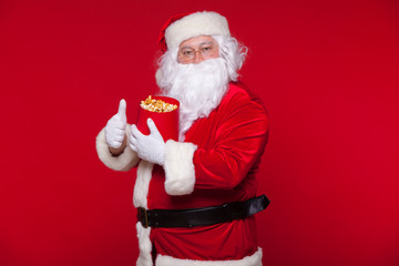 Traditional Santa Claus watching TV, eating popcorn. Christmas. Red background. emotions fear surprise