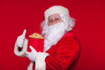 Traditional Santa Claus watching TV, eating popcorn. Christmas. Red background. emotions fear surprise