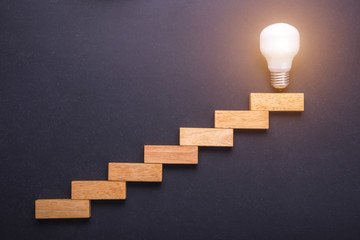 Wooden block set up for staircase with light bulbs on the top point on black stone board. Business success and create idea concept - obrazy, fototapety, plakaty