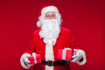 Christmas. Photo Santa Claus giving xmas present and looking at camera, on a red background
