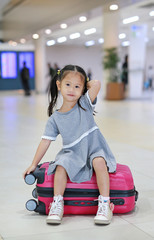 Adorable little asian girl at airport sitting on suitcase.