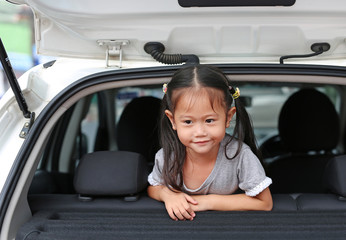 Smiling Asian child girl lying in the hatchback door of the car.