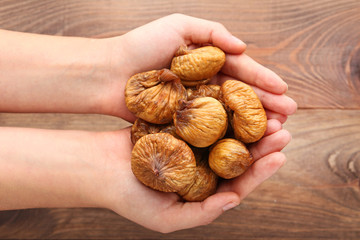 Dried figs in female hands on brown background