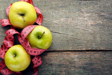 Measuring tape with green apples on wooden table