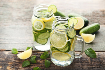 Lemonade with cucumbers, lemons and mint leafs in glass jars on wooden table