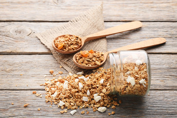 Tasty granola in spoons and glass jar on grey wooden table