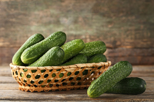 Fresh cucumbers in basket on grey wooden table