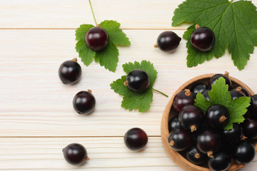 black currant in wooden bowl with green leaf on white wooden background. top view with copy space