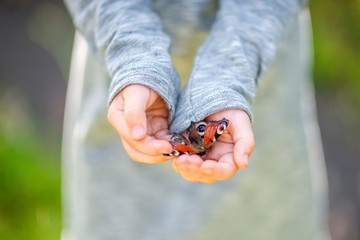 happy little girl is walking in a beautiful park holding a butterfly on her hands.