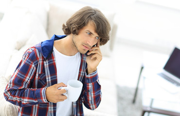 beautiful guy with a cup sits in front of a laptop.