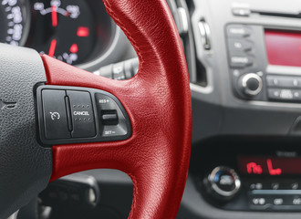 Cruise control buttons on the red steering wheel of a modern car, car interior details