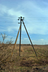 Fototapeta na wymiar Pole and crossarms support electrical wires in rural setting, blue cloudy sky and rotten grass background, spring day, Ukraine