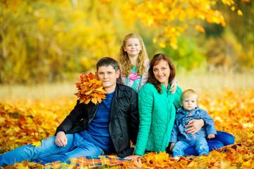 Fototapeta premium happy family walks in a beautiful autumn park, they sit on fallen leaves and smile.