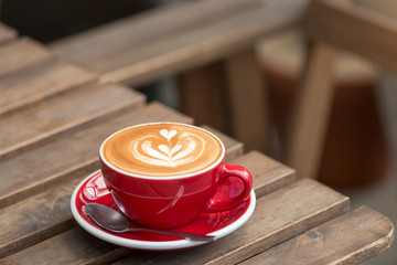 A red cup of hot latte coffee with latte art on the wooden table background.
