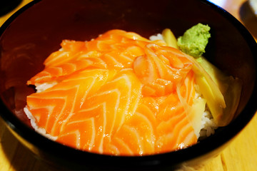 Japanese food salmon sashimi with rice in black bowl on wood table background