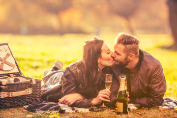 Young lovely happy couple -  lovers have a picnic in autumn park. Happy couple clinking and kissing...
