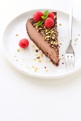 Fototapeta na wymiar Chocolate cheesecake or slice of chocolate cream pie decorated with raspberries and crushed nuts on white background