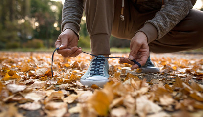 Man getting ready for running lacing sport shoes. Male in nature jogging on dried leaves.