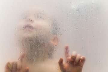 Baby in the shower behind glass with drops