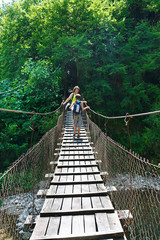 Mom and his son tourists cross the mountain river on a suspension bridge