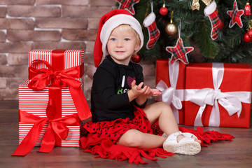 Christmas beautiful cute baby girl posing in casual clothes close to new year pine green tree with presents pillows and toy horse in studio scene