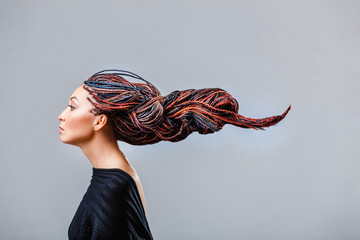 Modestudio-Shooting einer gemischtrassigen Frau mit einer kreativen bunten Frisur in Form eines aus Dreadlocks geflochtenen Zopfs in der Technik von Zizi. Das Konzept der Friseurkunst
