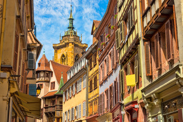 Ansicht einer Häuserfront mit alten Fachwerkhäusern und bunten Fensterläden und einen schönen Blick auf die Kathedrale im Hintergrund in der schönen alten französischen Stadt Colmar im Elsass.
