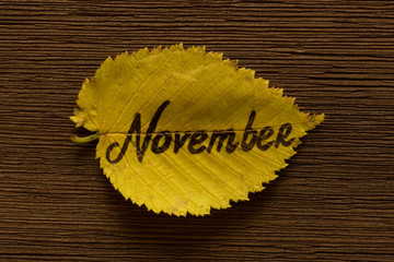 Naklejka premium Golden linden leaf with the inscription NOVEMBER on the brown wooden background. Close up.