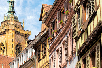 Ansicht einer Häuserfront mit alten Fachwerkhäusern und bunten Fensterläden und einen schönen Blick auf die Kathedrale im Hintergrund in der schönen alten französischen Stadt Colmar im Elsass.