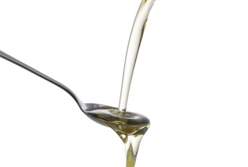 Olive oil poured from a bottle into a spoon isolated on white background