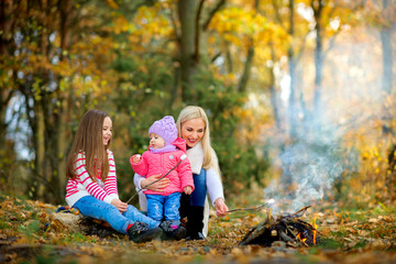 Fototapeta premium happy mother with two daughters in a beautiful autumn park, fry marshmallows at the stake.