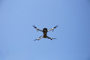 Small foldable drone flying viewed from below on a blue sky 