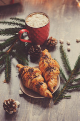 hot cocoa with marshmallows and croissant on rustic wooden table with christmas lights. Cozy winter home concept