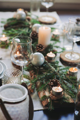 Festive Christmas and New Year table setting in scandinavian style with rustic handmade details in natural and white tones. Dining place decorated with pine cones, branches and candles