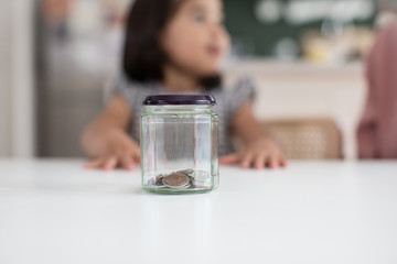 Jar with pocket money on table while girl sitting in background