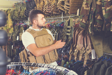 Young guy choosing flak jacket in military shop