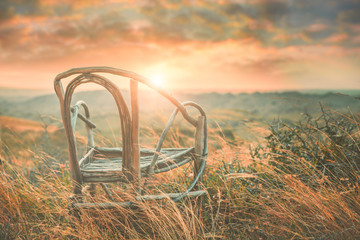 A chair is situated on the hill when the sunset with the silhouette scene.