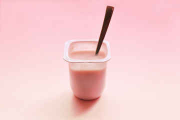 Strawberry yogurt or pudding  in white plastic cup on pink background with copy space. Raspberry pink yoghurt with spoon in it. Minimal style.