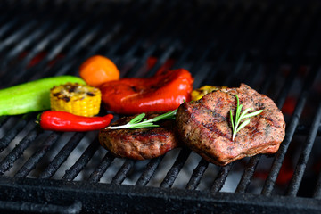 Delicious vegetables and meat grilling on open grill, bbq. Hot spicy steak grilling on a barbecue over the flaming hot coals garnished with a whole red  pepper and fresh rosemary. 