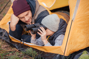 father and son with binoculars in tent