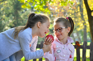 Two girls eat apples and play in autumn park. Children eating apples outdoors